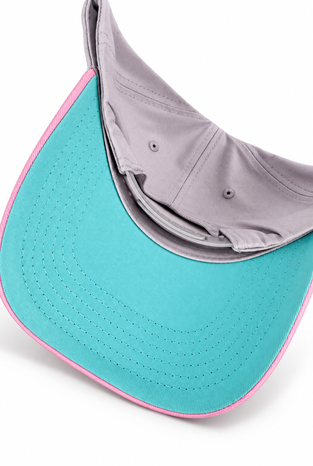A close-up of a baseball cap showing the underside of a turquoise visor with a pink stitched edge, layered over a light gray fabric lining.