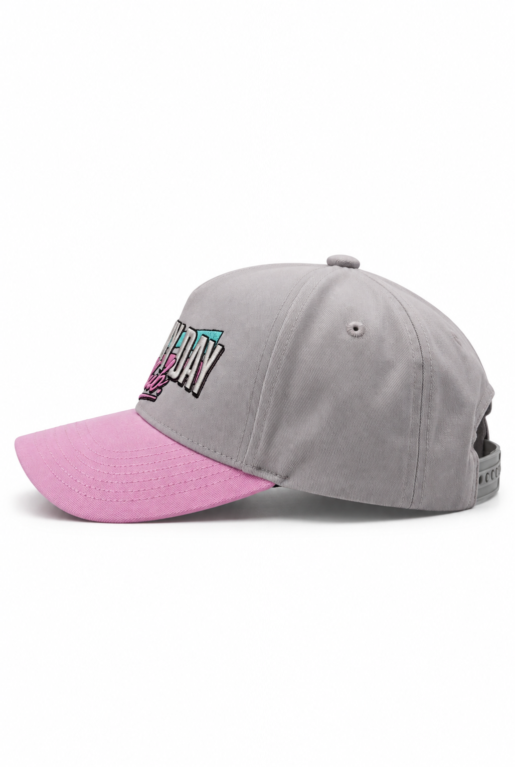 A gray baseball cap with a contrasting pink visor, featuring a colorful embroidered graphic on the front that reads 'BE DAY' in black, pink, and teal.